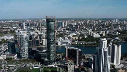 Tall buildings with blue windows taken from a drone. Stock footage. A magnificent landscape of a big city with beautiful houses and parks around the river.