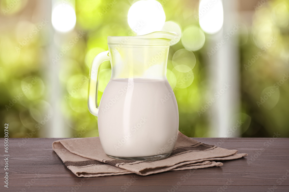 Fresh milk in glass pitcher on wooden table in room Fresh milk in glass pitcher on wooden table in room