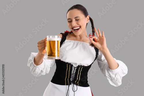 Young woman in traditional German clothes with beer showing OK on grey background