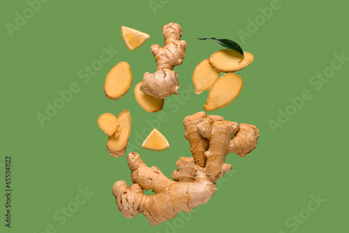 Flying slices of fresh ginger root and lemon on green background