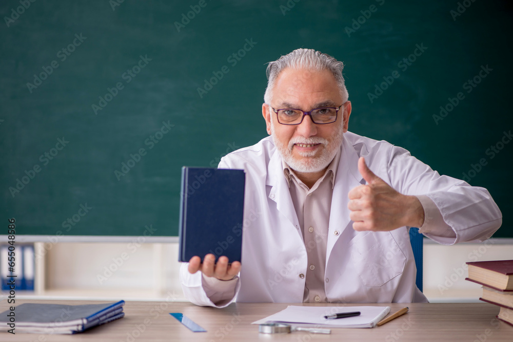 Old male teacher in front of green board Old male teacher in front of green board