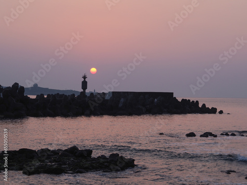 During the twilight hours at Shimen Cave in New Taipei City, the backdrop features a crimson setting sun, while in the foreground lies a breakwater made of tetrapods to mitigate waves.