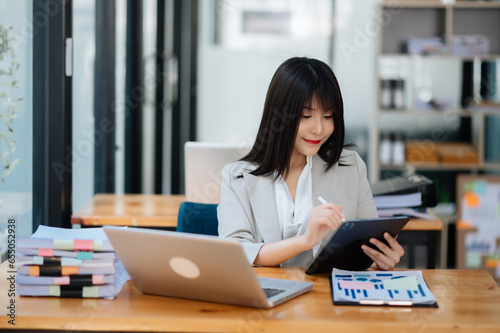 Successful Asian Businesswoman Analyzing Finance on Tablet and Laptop at Office Desk tax, report, accounting, statistics, and analytical research concept