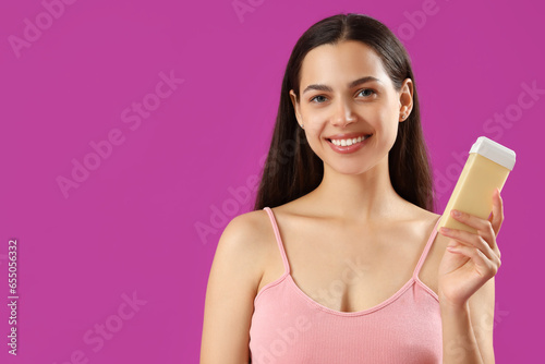 Happy beautiful young woman with liposoluble wax cartridge for epilation on purple background photo