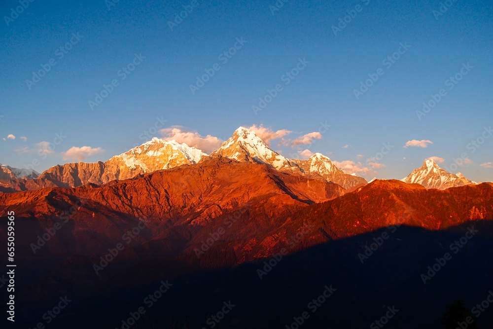 Vibrant hues of red and gold paint the majestic Annapurna ranges and iconic Mt. Machapuchare during a breathtaking sunset as seen from the enchanting Poon Hill in Nepal.