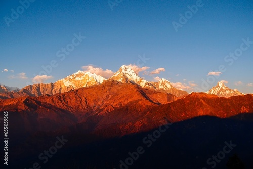 Vibrant hues of red and gold paint the majestic Annapurna ranges and iconic Mt. Machapuchare during a breathtaking sunset as seen from the enchanting Poon Hill in Nepal.