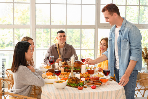 Group of young friends having dinner at festive table on Thanksgiving Day