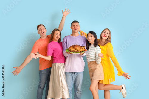 Group of young friends with tasty turkey on blue background. Thanksgiving Day celebration © Pixel-Shot