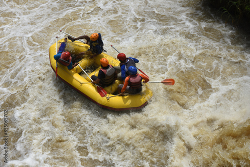 A group of tourists guided by a professional pilot on white water rafting, on a murky river after descending an extreme obstacle in the form of a waterfall on the Kesambon river, Malang, Indonesia
