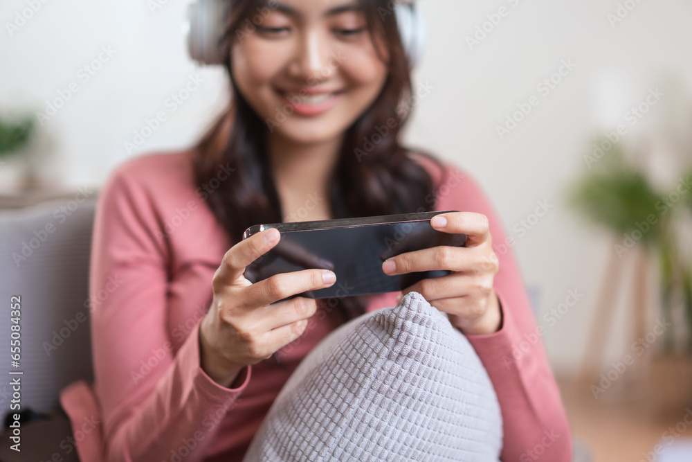 Women in headphone playing video games on smartphone while leisure on sofa in lifestyle at home Women in headphone playing video games on smartphone while leisure on sofa in lifestyle at home