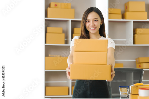 Confident Asian china people SME owner diligently packing products into boxes, epitomizing the e-commerce shift. As orders flood her inbox © M+Isolation+Photo