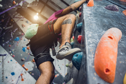 A strong male climber climbs an artificial wall with colorful grips and ropes.