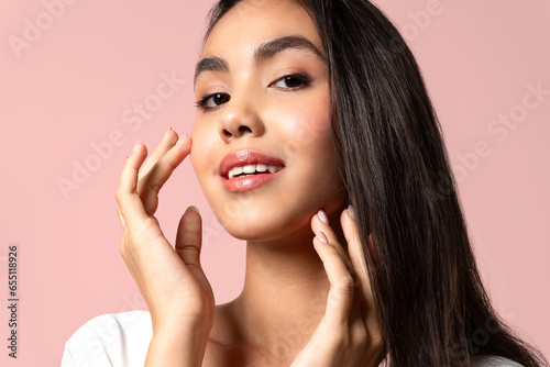 Beautiful asian woman with clean skin, natural make-up, and white teeth on pink background...