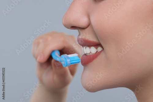 Woman brushing her teeth with plastic toothbrush on light grey background, closeup. Space for text
