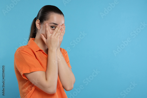 Embarrassed woman covering face on light blue background. Space for text photo