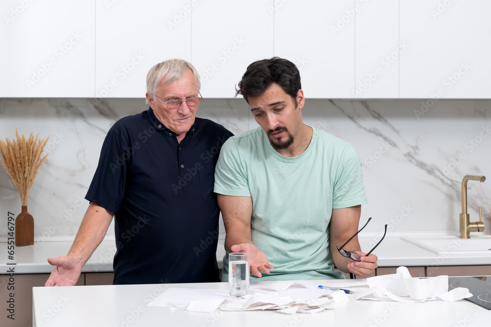 Close up of unhappy man and his elderly father sitting at the table, stressed and confused by calculate expense from invoice or bills, have no money to pay mortgage or loan Close up of unhappy man and his elderly father sitting at the table, stressed and confused by calculate expense from invoice or bills, have no money to pay mortgage or loan