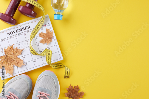 Fall physique makeover journey concept. Top view flat lay of calendar, dumbbells, stylish shoes, plastic water bottle, tape measure, dry maple leaves on yellow background with promo area