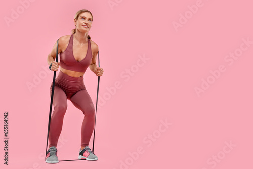 Woman exercising with elastic resistance band on pink background, low angle view. Space for text © New Africa