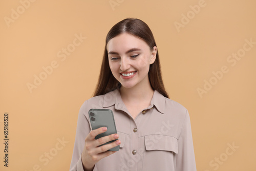 Smiling woman using smartphone on beige background