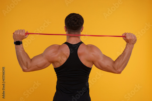 Young man exercising with elastic resistance band on orange background, back view photo