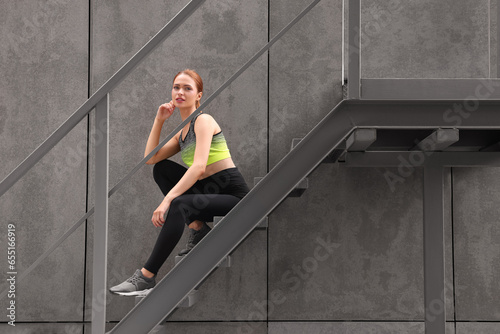 Beautiful woman in stylish gym clothes sitting on stairs on street