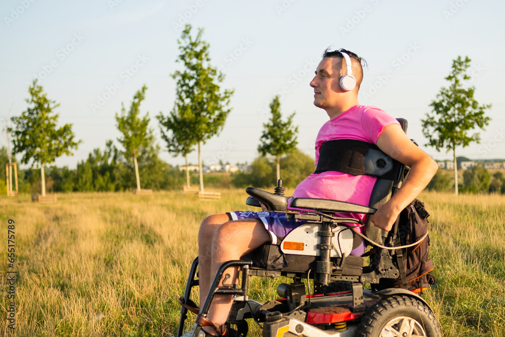 Gay man enjoys listening to music in white headphones. Sunlight illuminates man with neck tattoo sitting in wheelchair in green grassy meadow