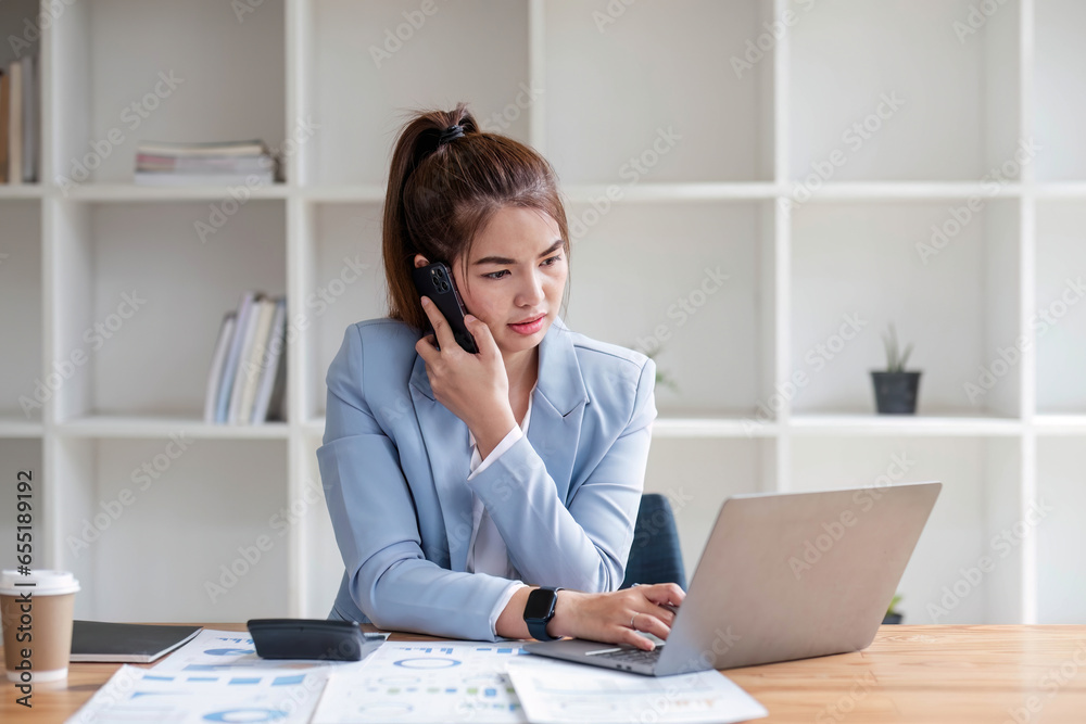 Attractive Asian woman using laptop in online meeting. Businesswoman using mobile phone talking with colleague sitting at table in modern office Attractive Asian woman using laptop in online meeting. Businesswoman using mobile phone talking with colleague sitting at table in modern office