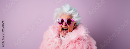 Colorful studio portrait of eccentric girly and feminine elderly granny wearing pink fur and sunglasses, pink background, excited expression
