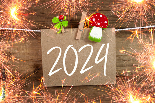 Wooden hang tag and slate with four leaf clover and sparklers with the german words for happy new year - frohes neues jahr 2024 on wooden weathered background photo