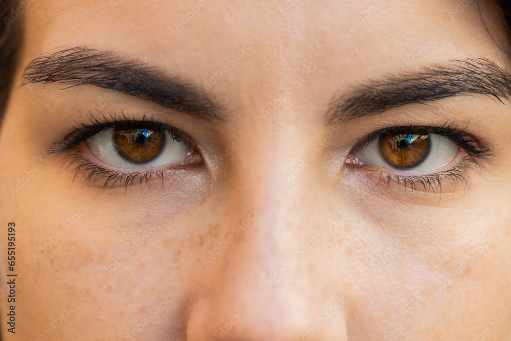 Obraz premium Extreme close-up macro portrait of smiling young adult Caucasian woman face. Brunette girl eyes, looking at camera. Dark brown eyes of lady. Portrait of positive female opening wide her closed eyes