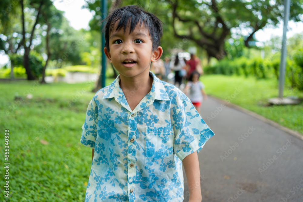Happy asian preschool boy walking in green tropical tree forest in city park Happy asian preschool boy walking in green tropical tree forest in city park