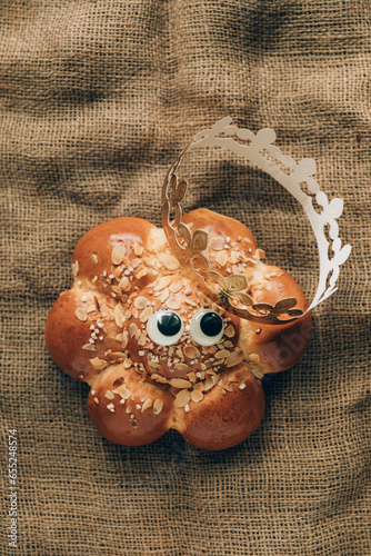 Three Kings Cake with a golden crown and a tiny king hidden inside. Swiss tradition to bake Dreikönigskuchen on January 6. Rustic sackcloth background, funny googly eyes.
