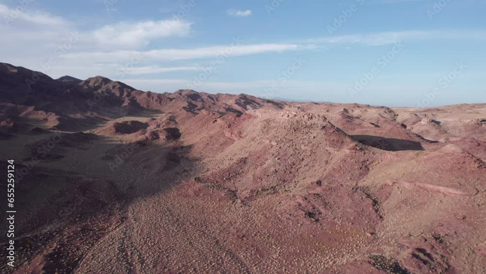 A white SUV is driving among the red mountains in the steppe. Dust flies behind the jeep. Bushes grow around. There are huge stones and many hills. Desert. The view from drone. Adventure. Kazakhstan A white SUV is driving among the red mountains in the steppe. Dust flies behind the jeep. Bushes grow around. There are huge stones and many hills. Desert. The view from drone. Adventure. Kazakhstan