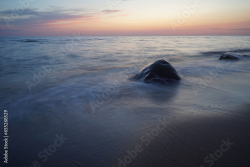 Sunset over the sea, lonely rock in water. Long exposure. Pastel background, blurry water, copy space.