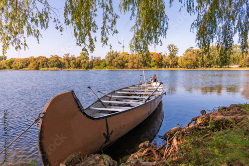 a large  voyageur canoe  full of paddles tied to the shore under weeping willow tree on toronto's center island shot on a sunny fall day