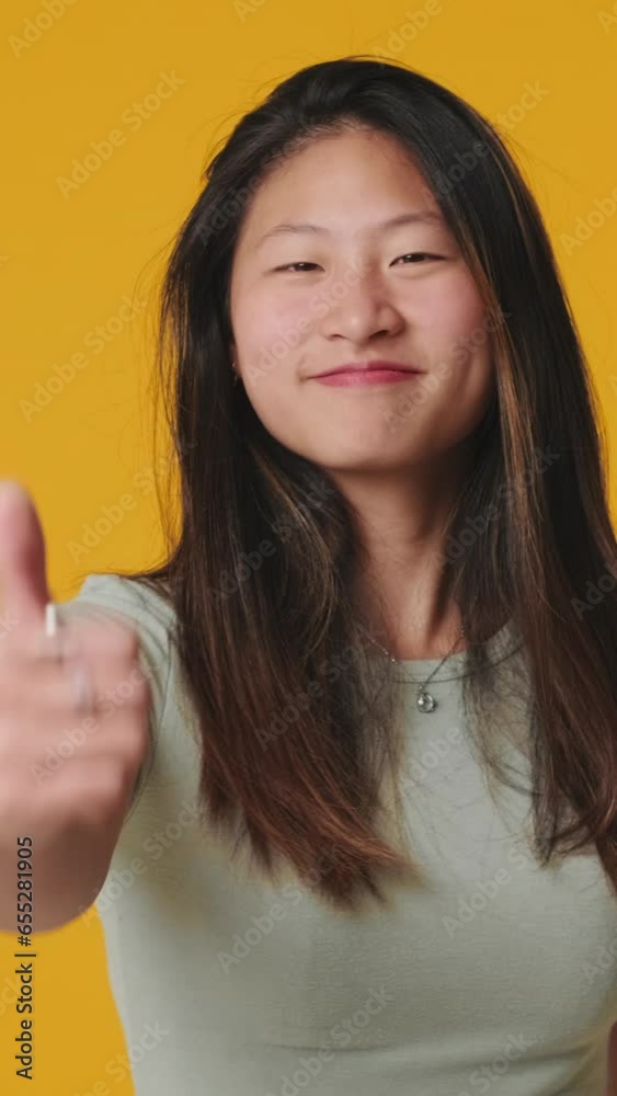 Young woman looking at camera showing thumbs up isolated on yellow background in studio Young woman looking at camera showing thumbs up isolated on yellow background in studio