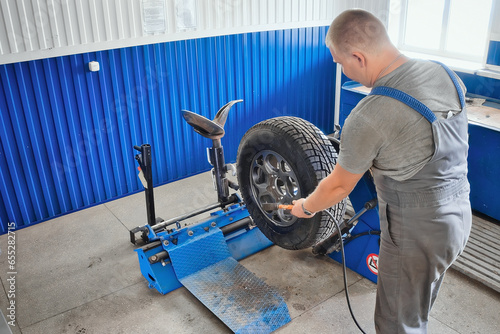 Car mechanic inflates car wheel with compressor in tire repair shop. Mechanic changes tires on wheel, balances and inflates tire. Professional car service.