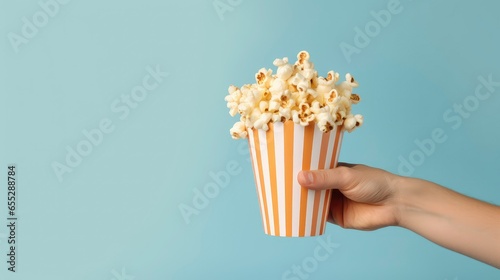 Hand holding striped bucket with popcorn on plain background photo