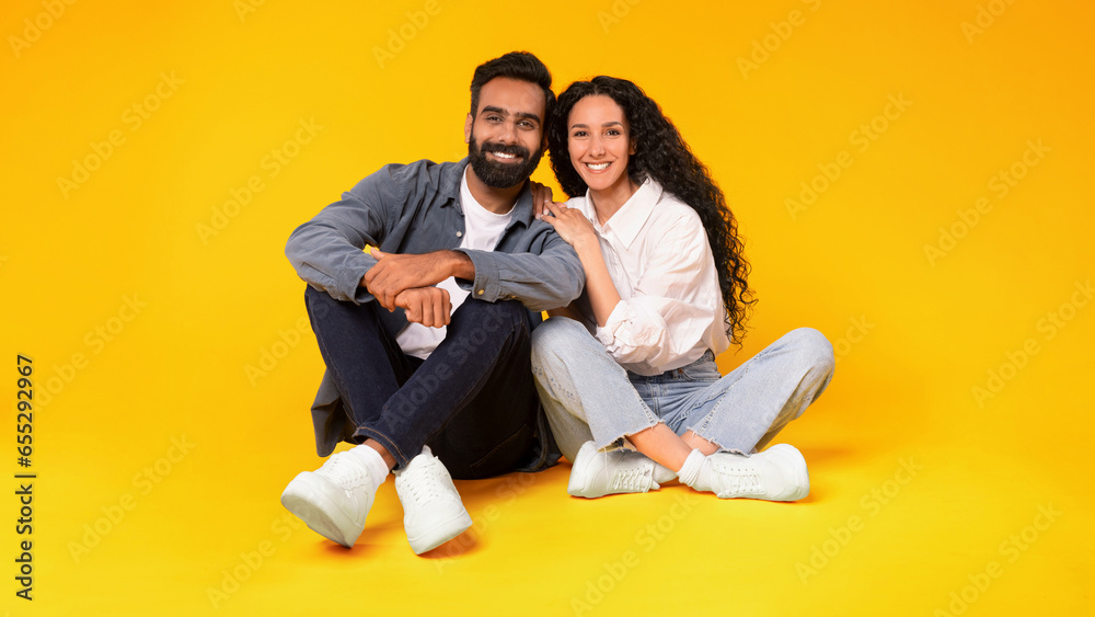 Loving Arabic Couple Embracing While Sitting Together Over Yellow Background Loving Arabic Couple Embracing While Sitting Together Over Yellow Background