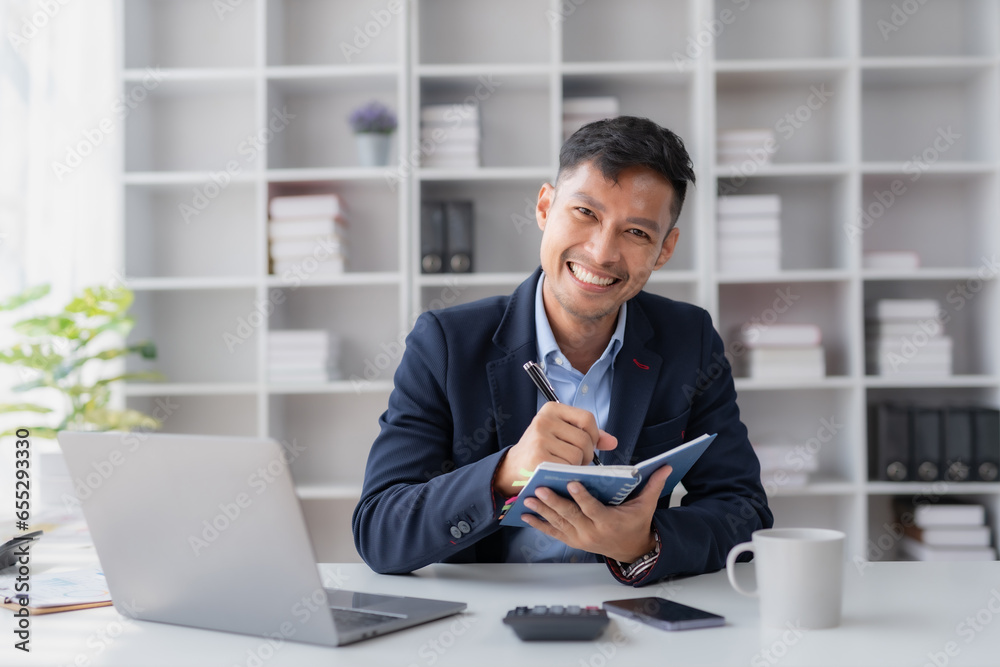 Fototapeta premium Handsome Asian businessman take notes and with laptop in the office.