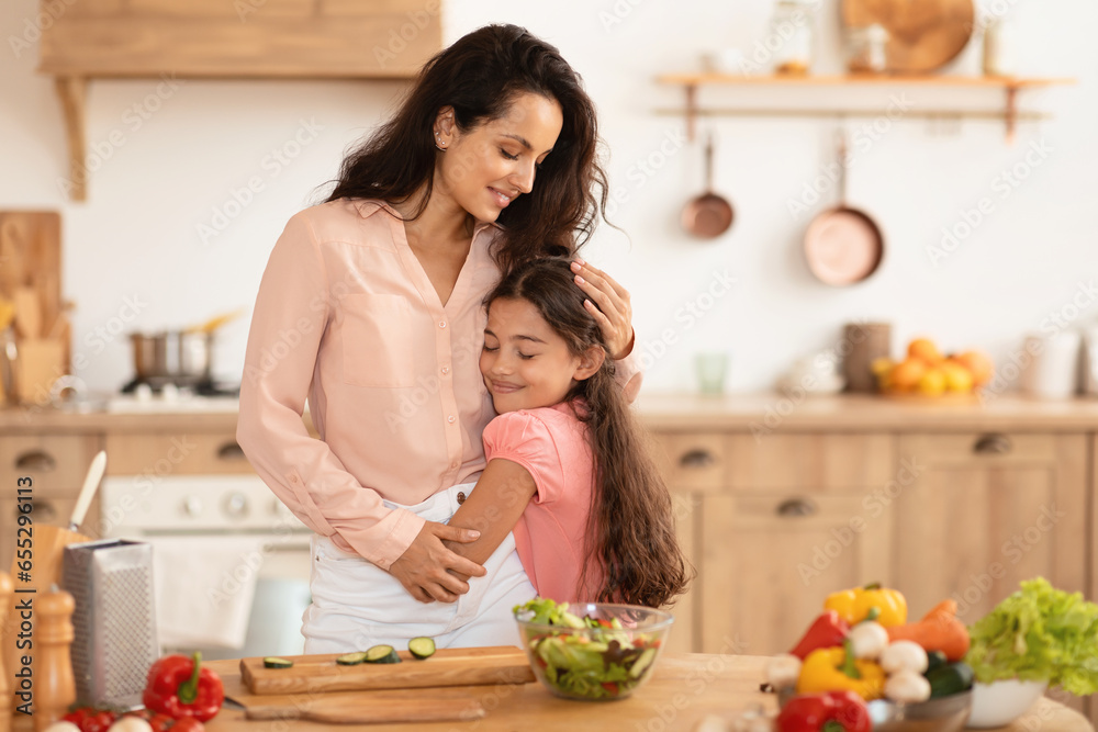 Loving mom embracing daughter while cooking together in modern kitchen