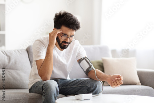 Sick Young Indian Man Checking Blood Pressure With Modern Tonometer At Home photo