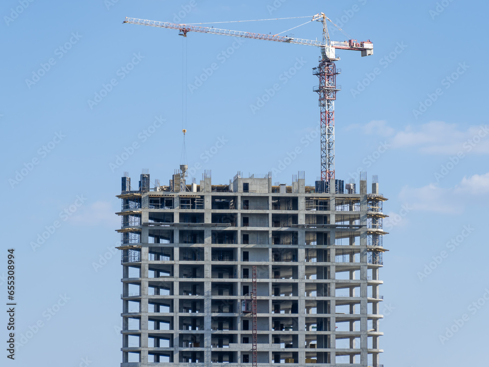 Fototapeta premium Industrial construction cranes work above new modern building. Engineering multistory design from concrete block and overlap. Development high-rise apartment with place for windows and balconys.