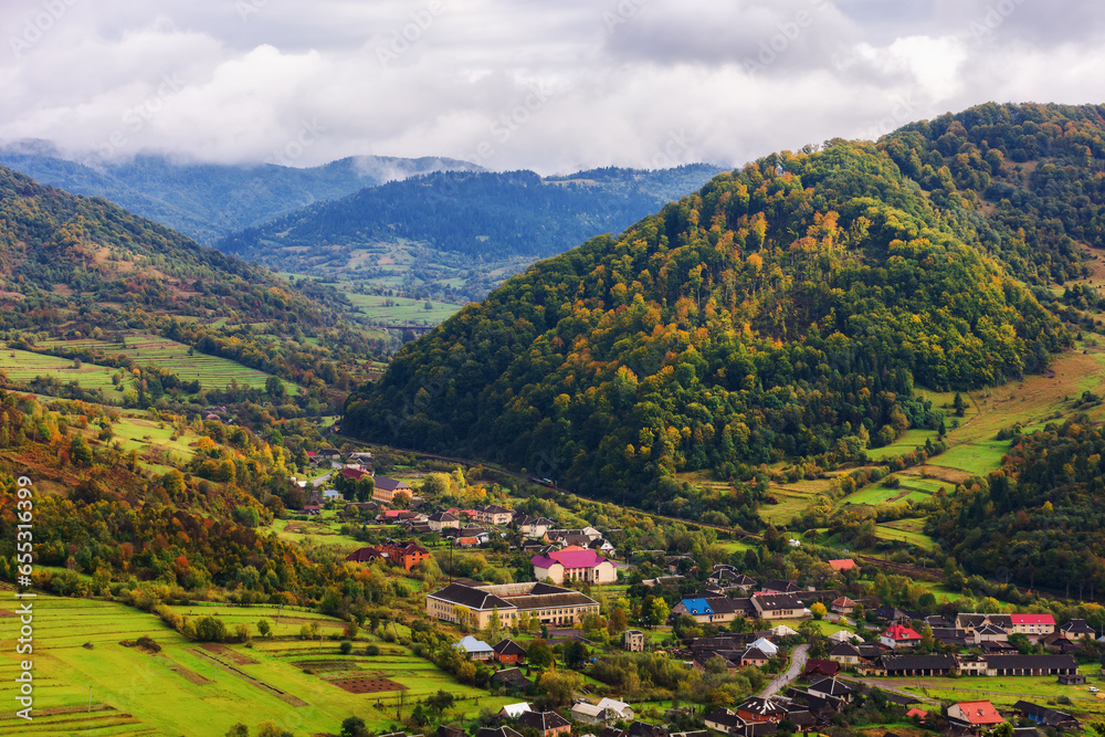 rural landscape of carpathian mountains. beautiful countryside scenery in autumn season with fields on the hills and village in the valley