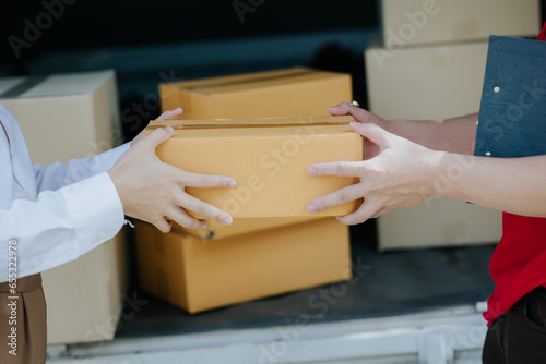 Young Asian woman receives a cardboard box from a smiling and happy delivery man at the front of the house. Asian male courier delivering goods to customers at doorstep © Witoon