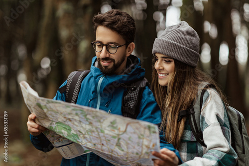 Smiling young caucasian lady and man in jackets look at route map, enjoy free time, walk