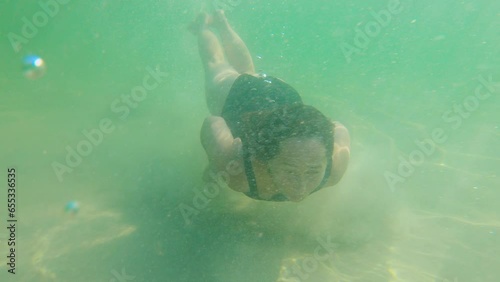 Beautiful woman, in a black swimsuit, swimming under the surface of the ocean with sandy bottom and sunlight, active healthy fitness lifestyle