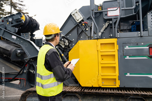 Engineer with digital tablet next to road construction machine