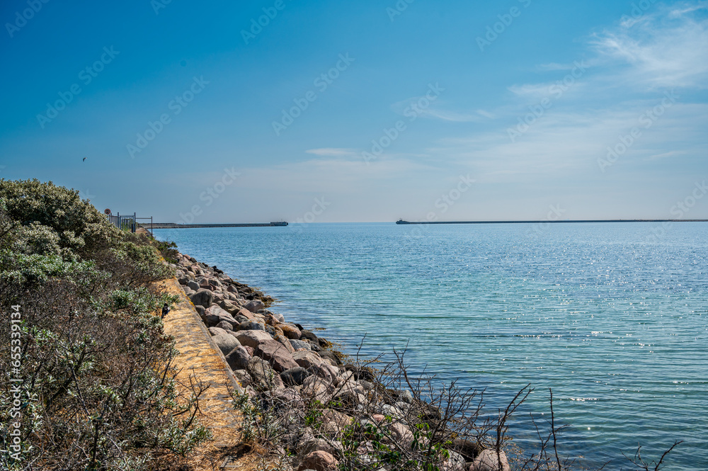 Fototapeta premium Blue sea with stone coast and pier in the distance