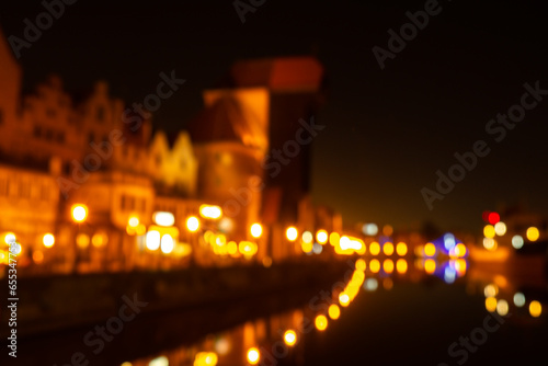 Defocused photo of Old town in Gdansk at night for greeting card background. The riverside on Granary Island reflection in Moltawa River Cityscape at twilight. Ancient crane at dusk. Visit Gdansk
